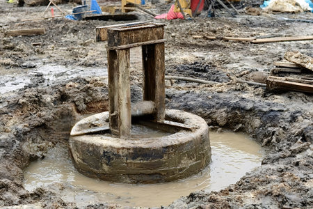 Construction machinery moving concrete piling in a muddy pit, laying groundwork and foundation at a building site, showing industrial development and excavationの写真素材