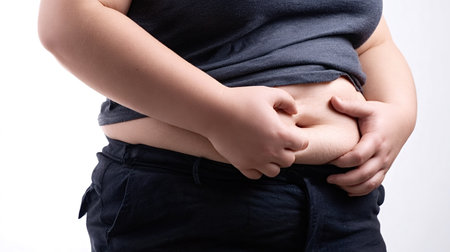 Person pinching abdominal skin, showing overweight midsection with visible stomach fat, representing challenges of body weight, diet, and general health on a white backgroundの写真素材