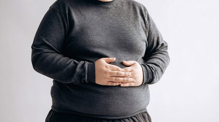 Overweight person holding their stomach and body, experiencing discomfort or pain, illustrating concepts of obesity, digestive issues, unhealthy lifestyle, and health problemsの写真素材