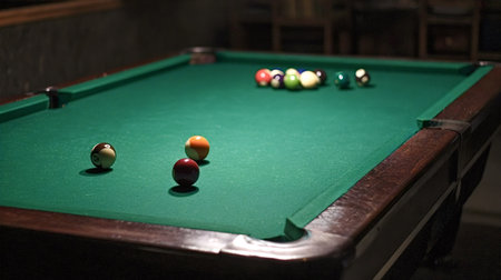 Billiard table displaying colorful pool balls racked and scattered on its green felt surface,...