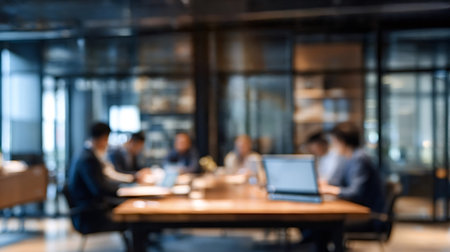 Corporate team sitting at a table with laptops, discussing business strategies in a blurred modern...