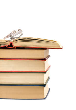 Open book and glasses lying on a pile of books on a white backgroundの写真素材