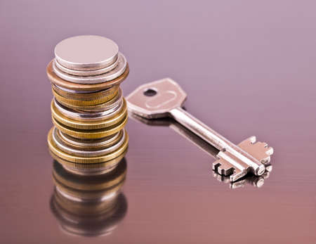 Stack of coins and a key on a gray background with reflectionの写真素材