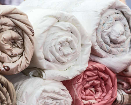 Rolled quilts and blankets of different colors.