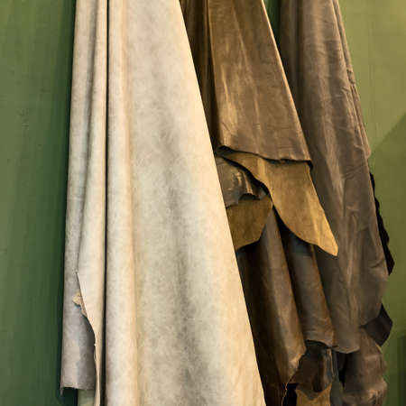 Part of many colors of leather sheets hanging on green wall background for sale in leather shop.