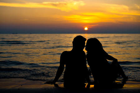 Silhouette of a young couple in love holding each other in front of the sea with sunset in the backgroundの写真素材
