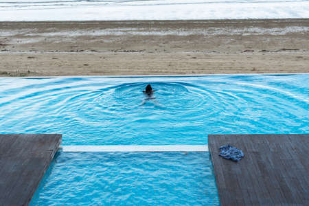 The waves at the surface of the water in the outdoor pool and the beach by the sea have children splashing in the pool.の写真素材