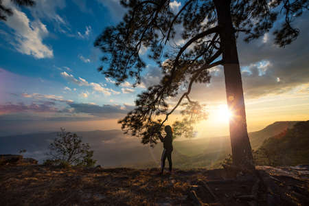 The silhouette of a female traveler is excited by the sunset view at Phu Kradueng, Loei Province, Thailand.の写真素材