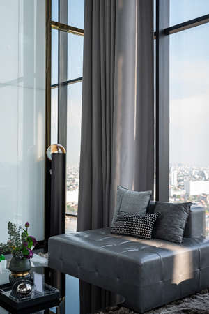 A large square sofa and three pillows in the living room on the 29th-floor luxury apartment. There is a bare glass wall overlooking the city.のeditorial素材