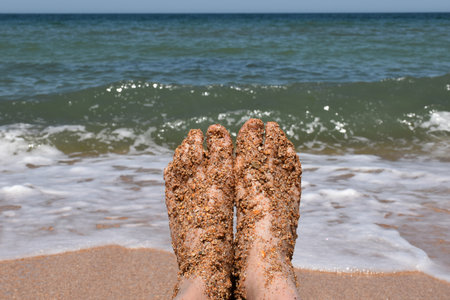 men's legs against the background of the sea surf on a sandy beach.の写真素材