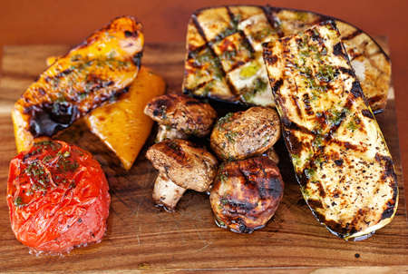 Grilled vegetables on cutting board on dark wooden background