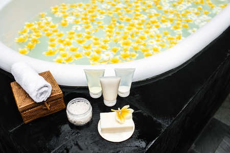 Shampoo, conditioner, shower gel, sea salt, towel and solid soap on a bathtube. Natural organic products. Take a relaxing bath with frangipani flower.の写真素材