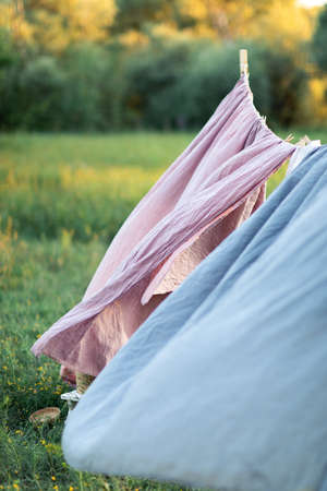 Pink and blue bedding sheet on forest background under the bright warm sun. Clean bed sheet hanging on clothesline at backyard. Hygiene sleeping ware concept.の写真素材