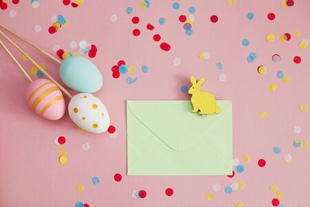 Easter eggs and envelope with easter bunny on a pink background with colorful confetti. Easter...