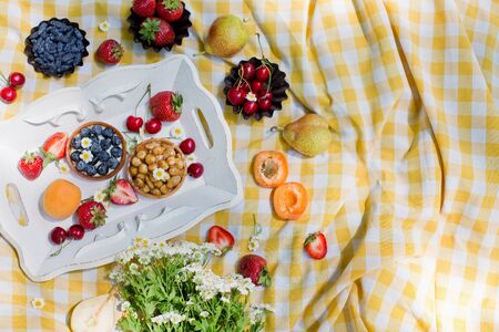 Picnic at the park. Fresh fruits and tarts with berries and nuts on the white wooden trayの写真素材