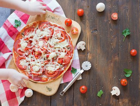 Child take homemade pizza with salami, onion, tomato and cheese. Pizza on a wooden backgroundの写真素材