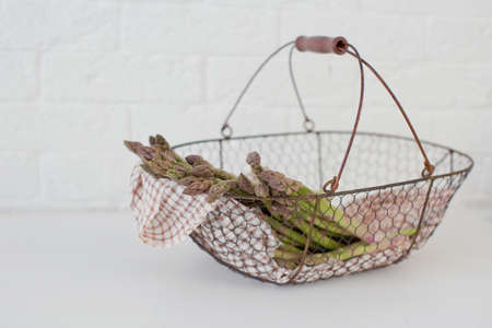 Fresh raw green asparagus in a metal vintage basket on a white brick wall background