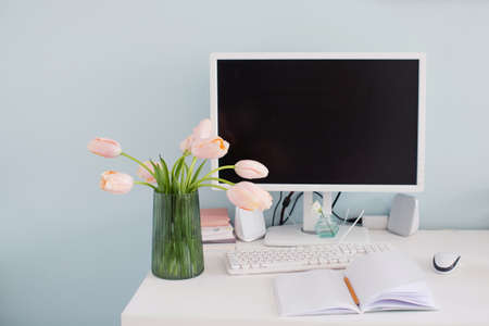 Modern workplace in light room with blue walls. Bouquet of pink tulips on the table. Feminine workspaceの写真素材