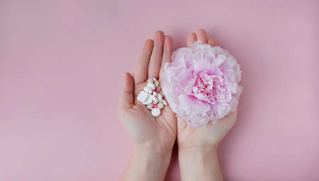Allergy concept. Pink peony and assorted pills in woman's hands on a pink background