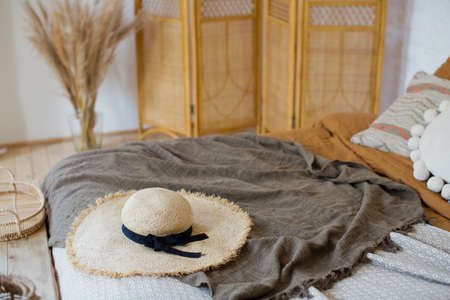 Straw hat on the bed bohemian bedroom. Boho bedroom with bed, pillows and blanketsの写真素材