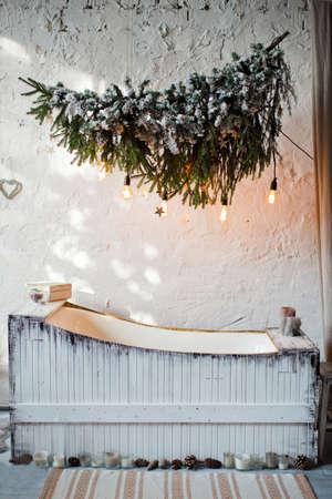 Wooden bathtub with Christmas tree branches and light bulbs decoration. Cozy winter batroomの写真素材