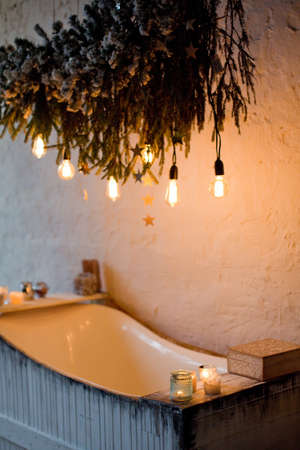 Wooden bathtub with Christmas tree branches and light bulbs decoration. Cozy winter batroomの写真素材