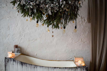 Wooden bathtub with Christmas tree branches and light bulbs decoration. Cozy winter batroomの写真素材