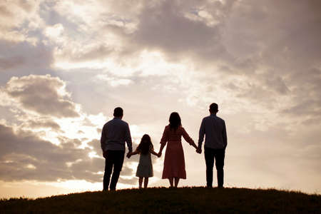 Silhouette of happy family. Man, woman, boy and girl holding hands and looking to the sunset skyの写真素材