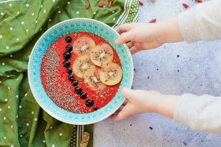 Smoothie bowl with kiwi, black berries and chia seeds and flax seeds on a light background. Child touch the bowl with smoothieの写真素材