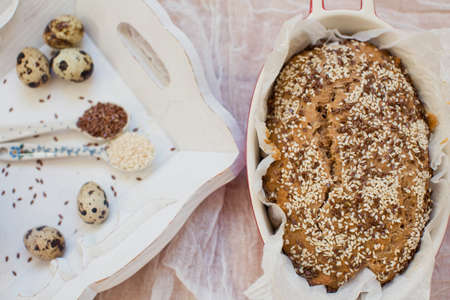 Whole wheat bread with sesame seeds and flax seeds in baking form on a light background. Fresh quail...