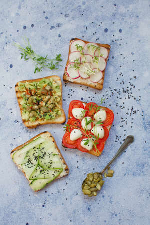 Healthy breakfast toasts. Wholegrain bread slices with cream cheese, avocado, radish, mozarella, cucumber, pumpkin seeds, sesame and microgreen on a blue backgroundの写真素材