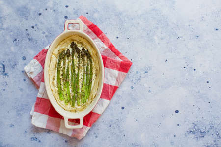 Pie with green asparagus and cream cheese in a baking form on a light blue backgroundの写真素材
