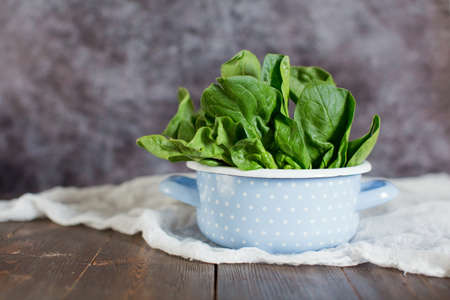 Fresh green spinach leaves in a blue vintage cooking pot on a wooden background