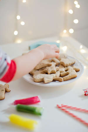 Christmas cookies on a white plate with colorful icing glaze. Childs hand take cookies. Christmas cookies background. Baked cookies, glaze in tubes, candy canes and lightsの写真素材