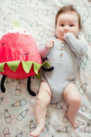 Baby boy with red strawberry toy lying on the bed