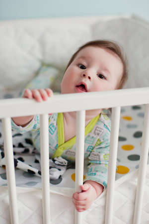 Little baby boy lying in his crib in light room and play with his toysの写真素材