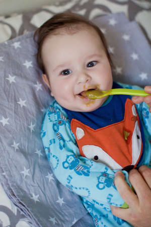 Little baby boy eat his first food from green spoon. Baby in cute bib eat vegetable pureeの写真素材