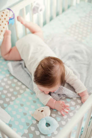 Little baby boy lying in his crib in light room and play with his toysの写真素材