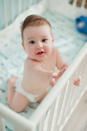 Little baby boy sitting in his crib in light room and play with his toysの写真素材