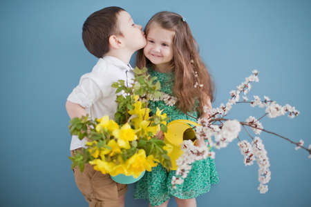 Toddler boy and girl holding daffodills and apricot blossom branches. Cute todler kids on blue...