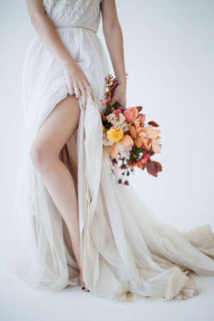 Bride walks in beautiful wedding dress with autumn colorful bouquet. Woman with autumn flowers on a white backgroundの写真素材