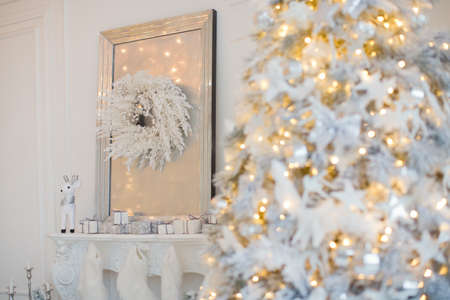 Cozy white Christmas interior room. Living room with Christmas tree, mirror with Christmas wreath, fireplace with socks and white and silver decorationsの写真素材