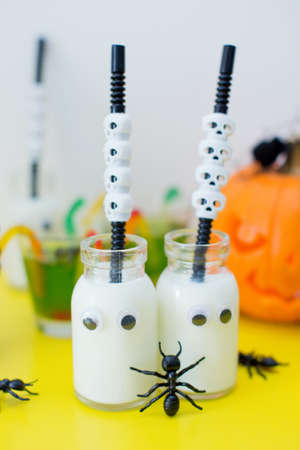 Halloween food, candy bar with sweets and carved pumpkin on a yellow table. Glass bottles with eyes and with milk inside and black big antsの写真素材