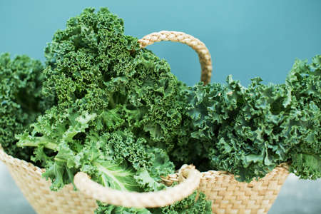 Green curly kale salad in straw eco bag on a blue backgroundの写真素材