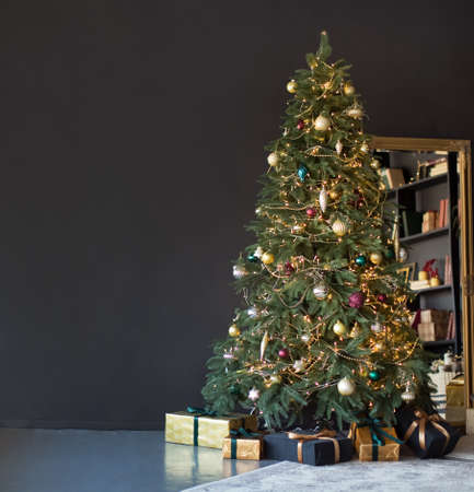 Banner Christmas tree with golden decorations and lights near black wall and vintage miracle in dark interior with copy space, place for textの写真素材