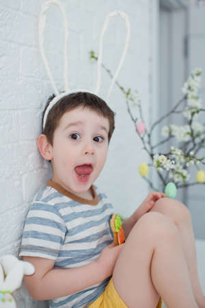 Caucasian toddler boy with funny bunny ears eat cookies. Boy with cookies near easter tree on a...