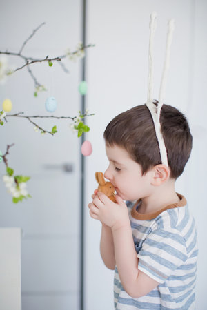 Caucasian toddler boy with funny bunny ears stands near easter tree with colorful eggs on a white backgroundの写真素材