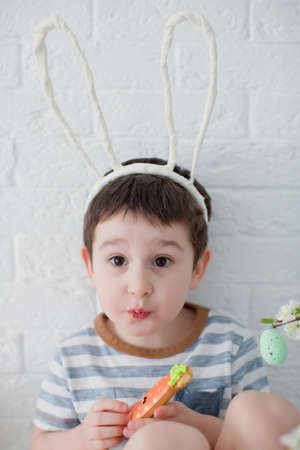 Caucasian toddler boy with funny bunny ears eat cookies. Boy with cookies near easter tree on a...