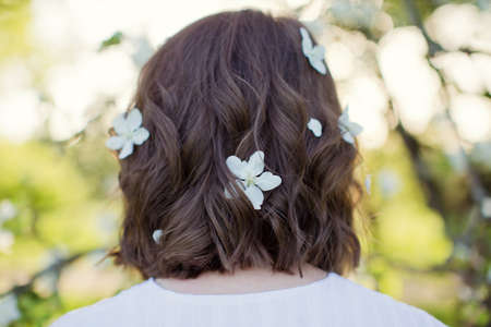Woman with white apple blossom flowers in the hair. Beautiful caucasian woman in white dress walks in spring blossom gardenの写真素材