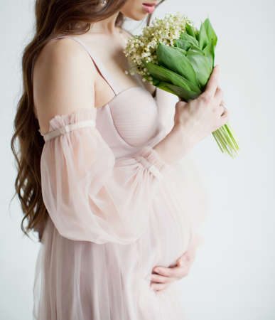 Pregnant woman in pink dress holds spring flowers lily of the valley on a white backgroundの写真素材